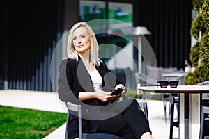 Blonde business lady looks at the phone, reading messages. Woman is relaxing in a cafe on the terrace enjoyment of life