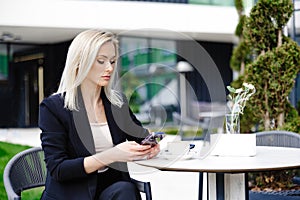 Blonde business lady looks at the phone, reading messages. Woman is relaxing in a cafe on the terrace enjoyment of life