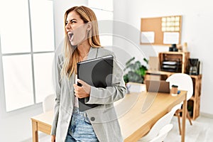 Blonde business woman at the office angry and mad screaming frustrated and furious, shouting with anger