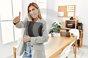 Blonde business woman at the office approving doing positive gesture with hand, thumbs up smiling and happy for success