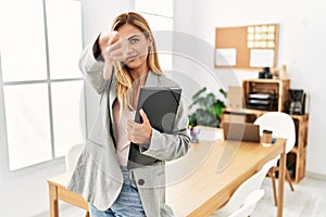 Blonde business woman at the office looking unhappy and angry showing rejection and negative with thumbs down gesture