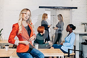 Blonde business woman smiles at camera with colleagues working in background