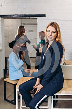 Blonde business woman smiles at camera with colleagues working in background