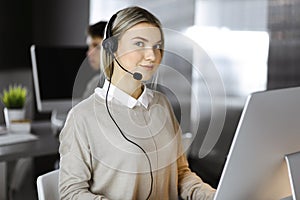 Blonde business woman talking by headset while sitting in modern call center office. Telemarketing and customer service
