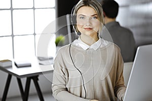 Blonde business woman talking by headset while sitting in modern call center office. Telemarketing and customer service