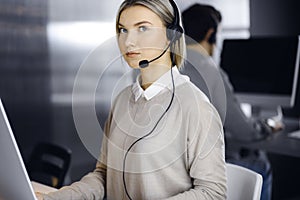 Blonde business woman talking by headset while sitting in modern call center office. Telemarketing and customer service