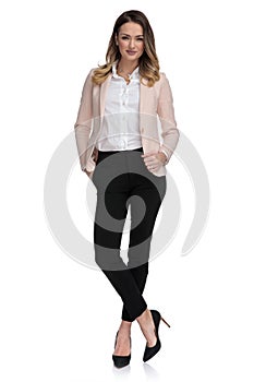 Blonde businesswoman stands cross-legged with hand in pocket