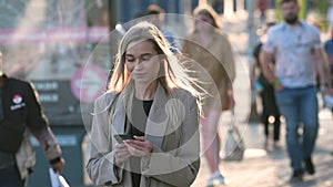 Blonde businesswoman walking on downtown streets while texting on smartphone.