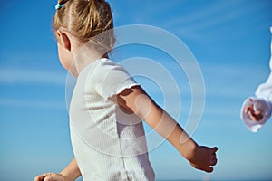 Blonde Caucasian child girl running against blue clear sky background. Happy carefree childhood. Kids. Children. Family