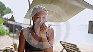 Blonde caucasian female surfer squeezing sunscreen on hand and applying it on her face. Tanned young surfing woman