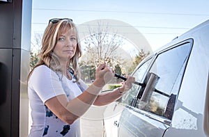 Blonde caucasian woman cleaning car windows at gas station