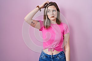 Blonde caucasian woman standing over pink background confuse and wondering about question