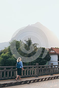 Blonde Caucasian woman walking on the bridge at sunset in Nong Khiaw, Laos