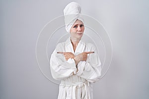 Blonde caucasian woman wearing bathrobe pointing to both sides with fingers, different direction disagree