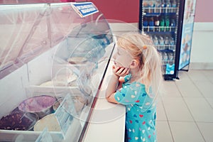 Blonde child girl looking at ice cream in shop window trying to choose one