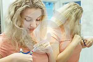 A blonde with curly hair cuts off the split ends with scissors.