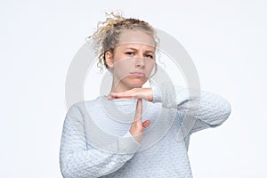 Blonde curly woman in blue sweater making time out gesture