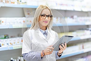 Blonde doctor in white uniform using tablet and technology in pharmaceutical or medical field