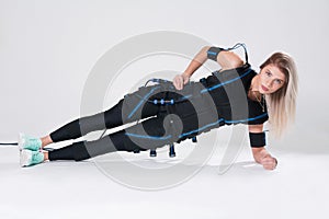 Blonde in an electric muscular suit for stimulation makes an exercise on the rug.