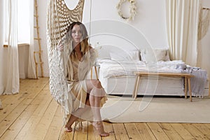 Blonde European female sitting on hammock in bright modern bedroom