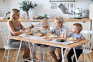 Blonde family mother with three kids two sons and daughter eating healthy food in kitchen at home, mom puts green salad