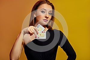 Blonde female with bright make-up, in black dress is showing two aces, posing against colorful background. Gambling