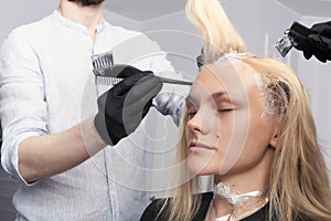 A blonde female client coloring hair in hairdressing salon