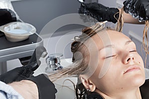 A blonde female client coloring hair in hairdressing salon