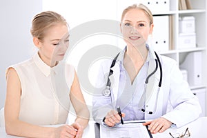 Blonde female doctor and patient talking in hospital office. Health care and client service in medicine