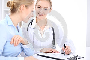 Blonde female doctor and patient talking in hospital office. Health care and client service in medicine