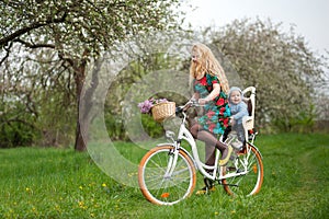 Blonde female riding city bicycle with baby in bicycle chair