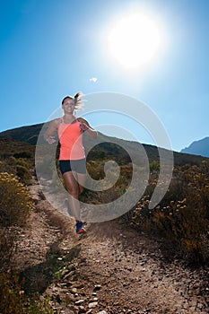 Blonde female trail runner running through a mountain landscape