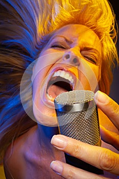 Blonde female vocalist under gelled lighting sings with passion into condenser microphone