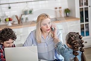 Blonde female working on laptop and talking on mobile, curly boy sitting next to her