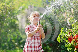 A blonde girl baby walks on a sunny day, takes care of the garden