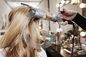 Blonde girl in a beauty salon doing a hairstyle. Twisting locks of hair on a styler. Close-up
