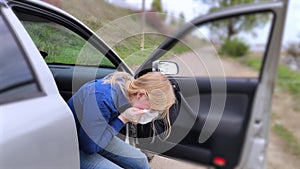 The blonde girl became ill from driving a car. Vomiting forced her to look out of the car so that the vomit would not enter the pa