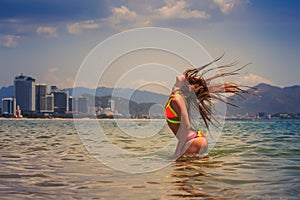 blonde girl in bikini stands in sea shaken head lifts hair up