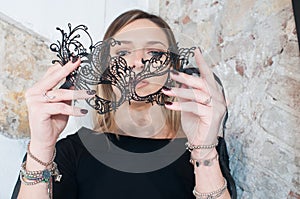 Blonde girl with black carnival mask over white background. Masquerade