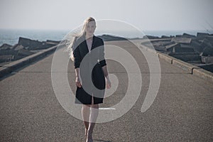 Blonde girl in a black coat at the pier