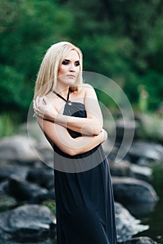 Blonde girl in a black dress with blue eyes on the coast of the river