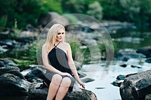 Blonde girl in a black dress with blue eyes on the coast of the river