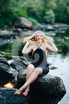 Blonde girl in a black dress with blue eyes on the coast of the river