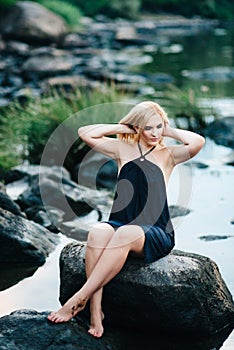 Blonde girl in a black dress with blue eyes on the coast of the river