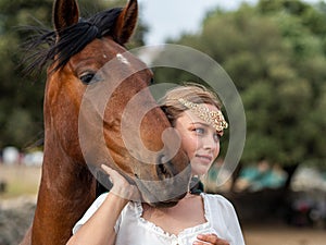 Blonde girl with blue eyes and makeup with elf in the field with a brown horse and a green cape