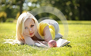 Blonde Girl with Book and Apple lying on Green Grass