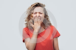 Blonde girl bored and yawning tired covering mouth with hand. Studio shot, white background. Restless and sleepiness