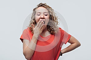 Blonde girl bored and yawning tired covering mouth with hand. Studio shot, white background. Restless and sleepiness