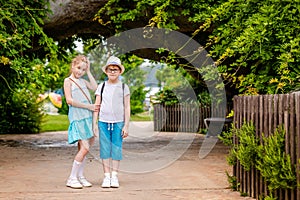 Blonde girl and boy in the hat and big glasses under the huge green tree