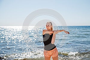 A blonde girl in a dark t shirt and light shorts does sports in the summer on the sea coast